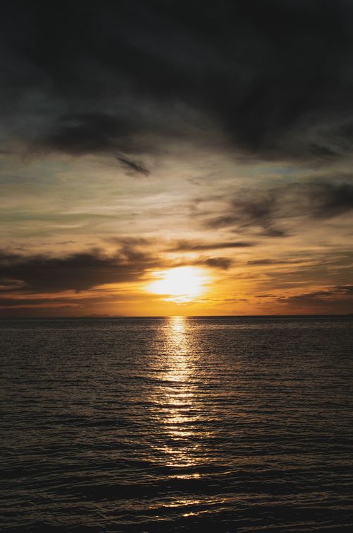 Free A captivating sunrise with dramatic clouds reflecting on calm ocean waters. Stock Photo
