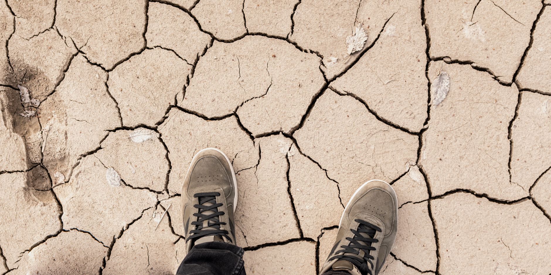 A person's feet wearing sneakers standing on cracked, dry, desert-like ground.