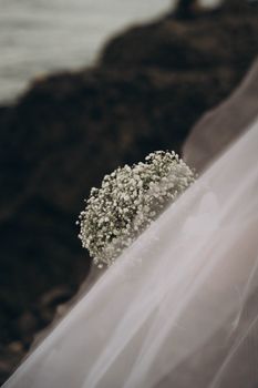 Close-up of a delicate bridal bouquet with veil near the sea, evoking romance.
