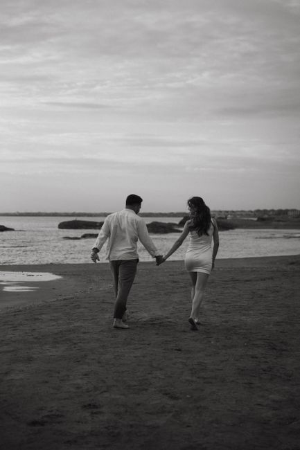Couple walking hand in hand along the beach in a black and white photo.
