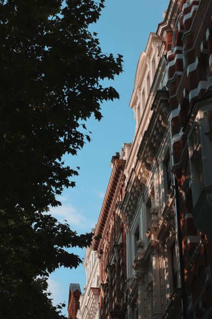 Elegant historic buildings in London with a backdrop of clear blue skies, showcasing distinctive architectural styles.