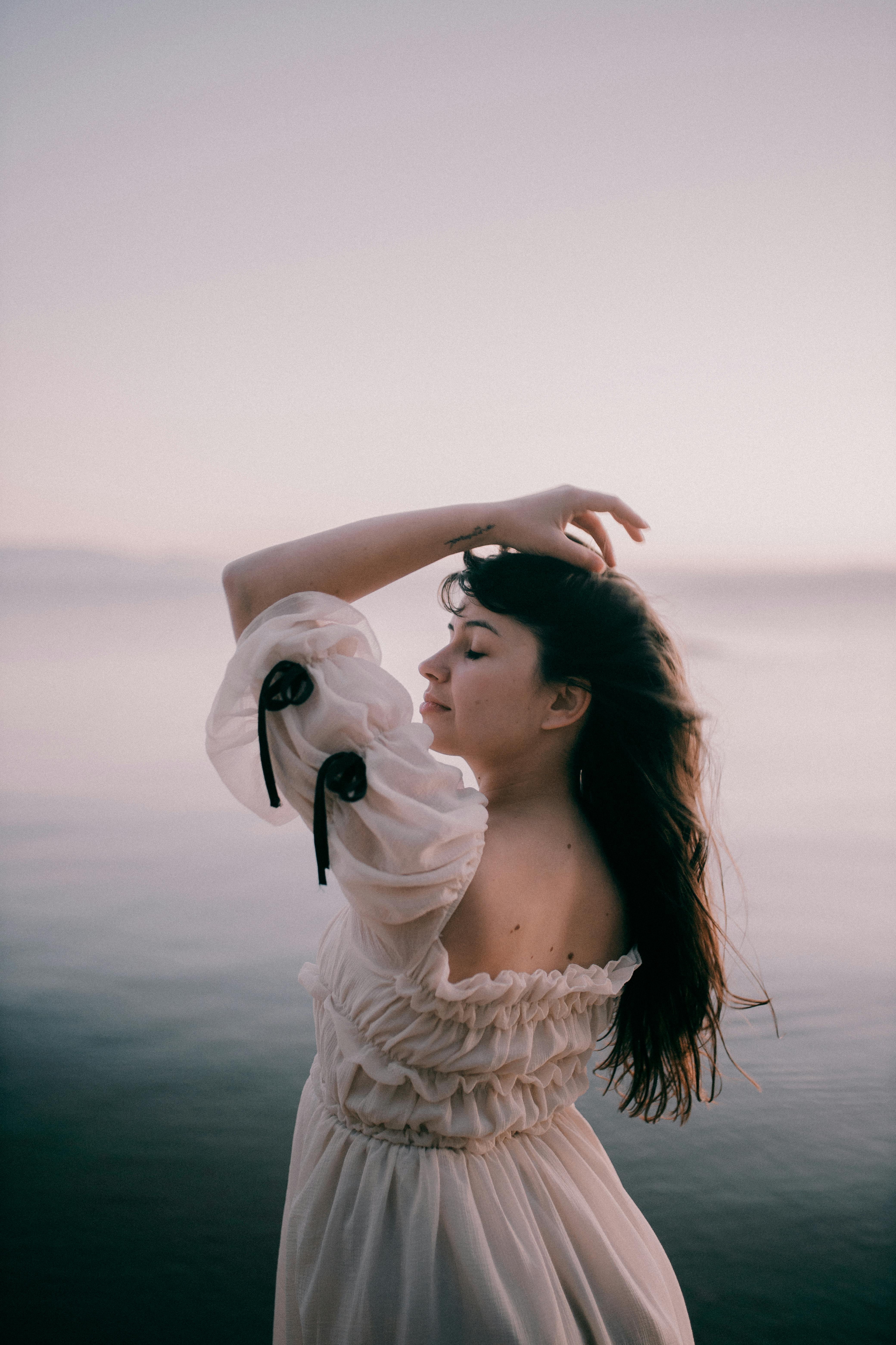 Elegant portrait of a woman standing by the sea during sunset. Featuring a peaceful and artistic vibe.
