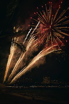 Spectacular fireworks illuminate the night sky in Honolulu, Hawaii, with palm trees in silhouette.