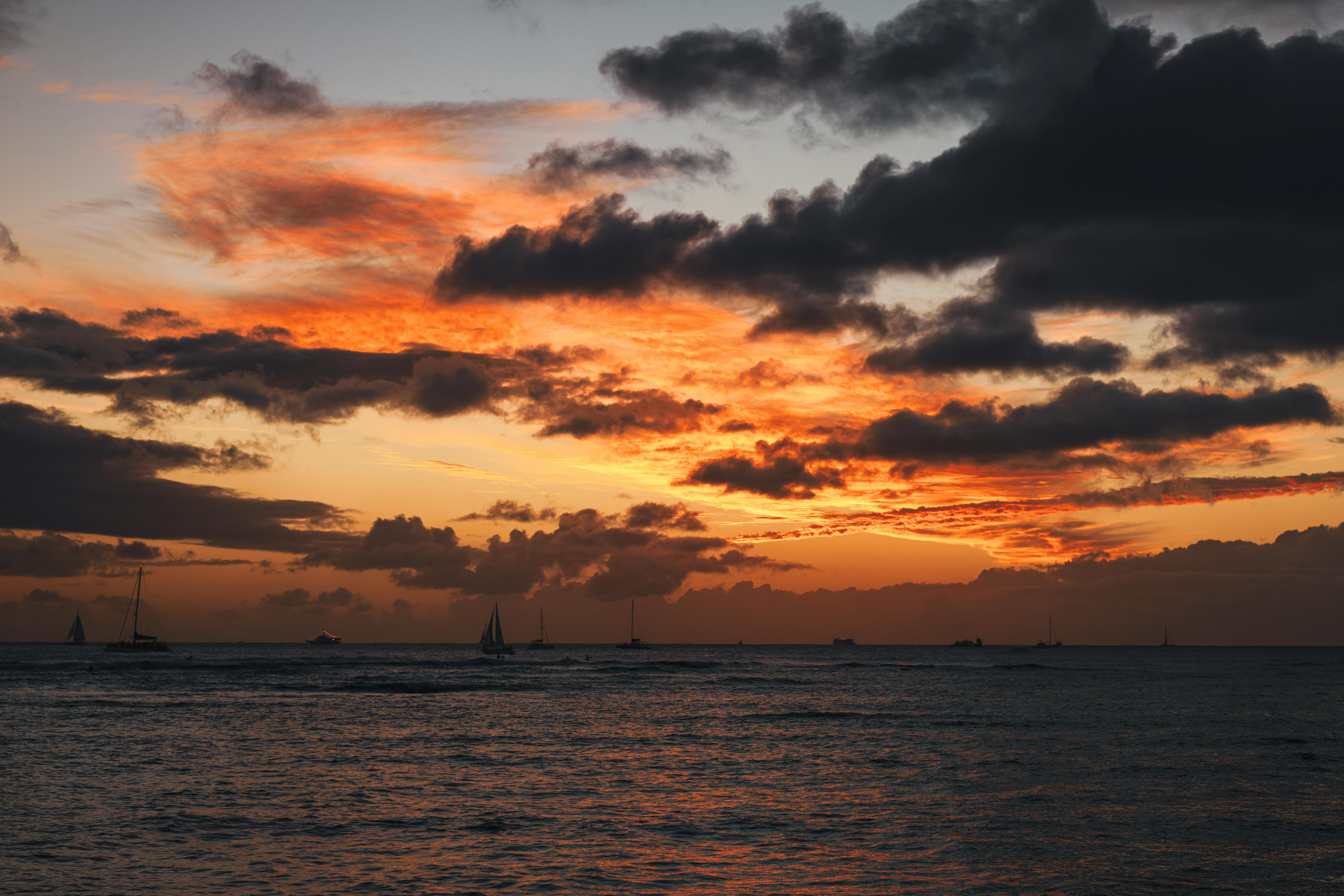 Beautiful sunset over the ocean with vibrant clouds and sailboats.