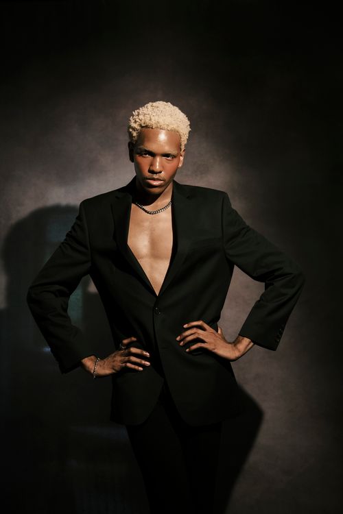 Free Elegant studio shot of a stylish model in a black suit posing confidently with dramatic lighting. Stock Photo