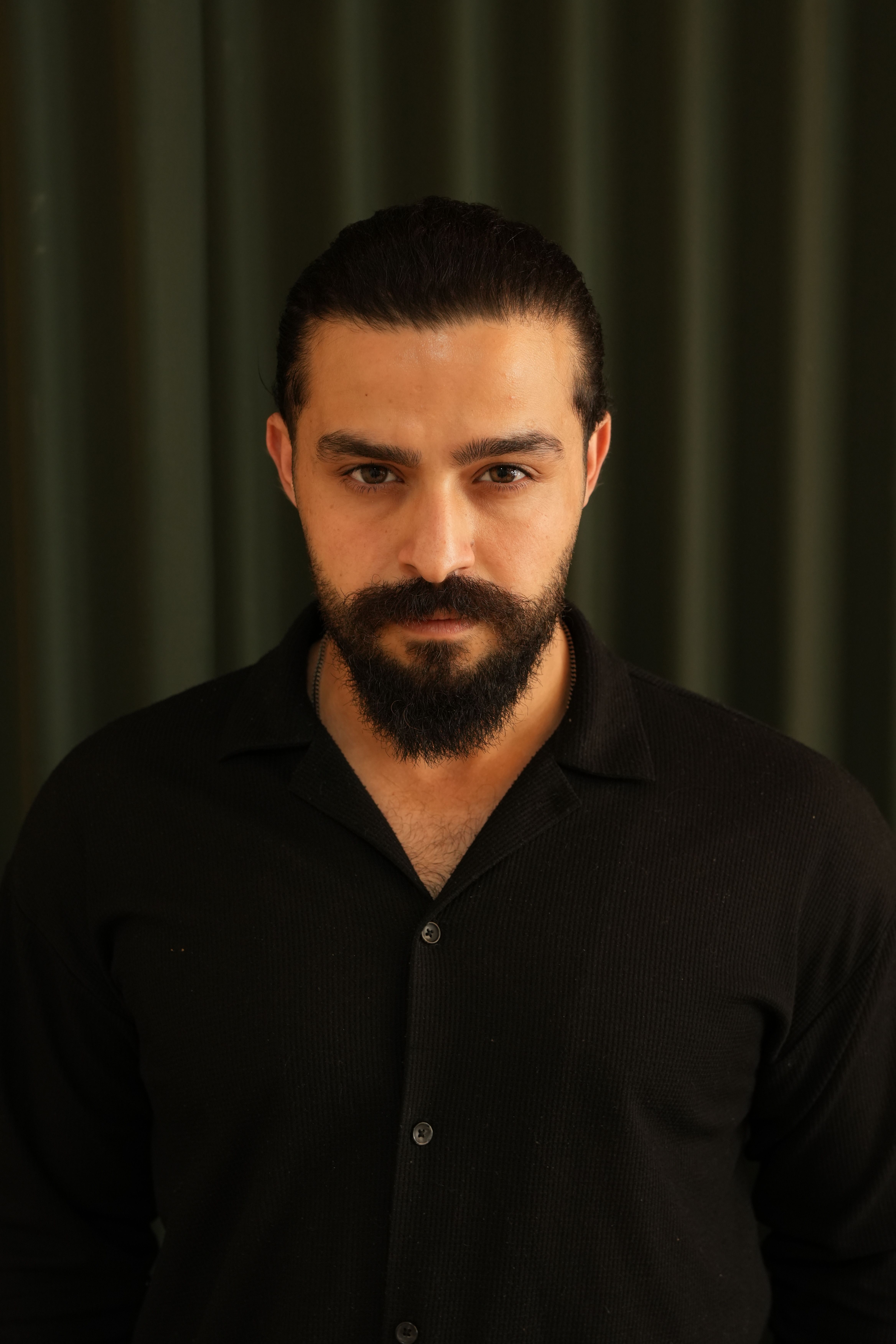 A striking portrait of a man with a beard and mustache wearing a black shirt, captured in a studio setting.