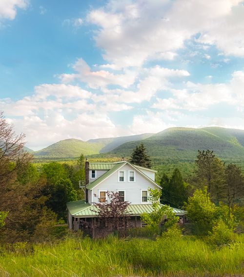 Free Charming house nestled in a verdant valley with mountain views under a bright sky. Stock Photo