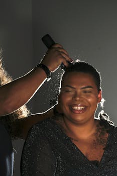 A person enjoys a joyful moment during a hair styling session indoors, showcasing laughter and warmth.