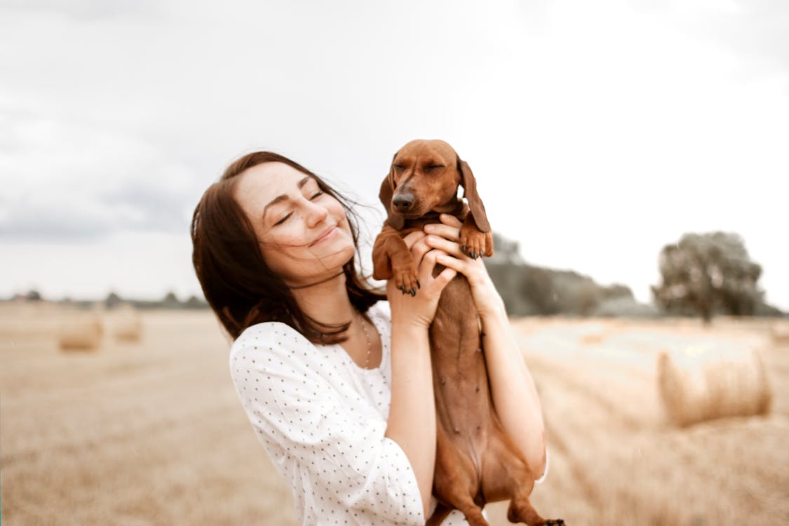 Smiling Woman Carrying Brown Dachshund