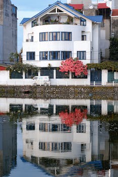 Stunning white house with blue accents reflecting in a calm river.