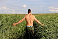 一名肌肉发达的男子走过郁郁葱葱的绿地，欣赏着乡村的宜人风光和天空的优美景色