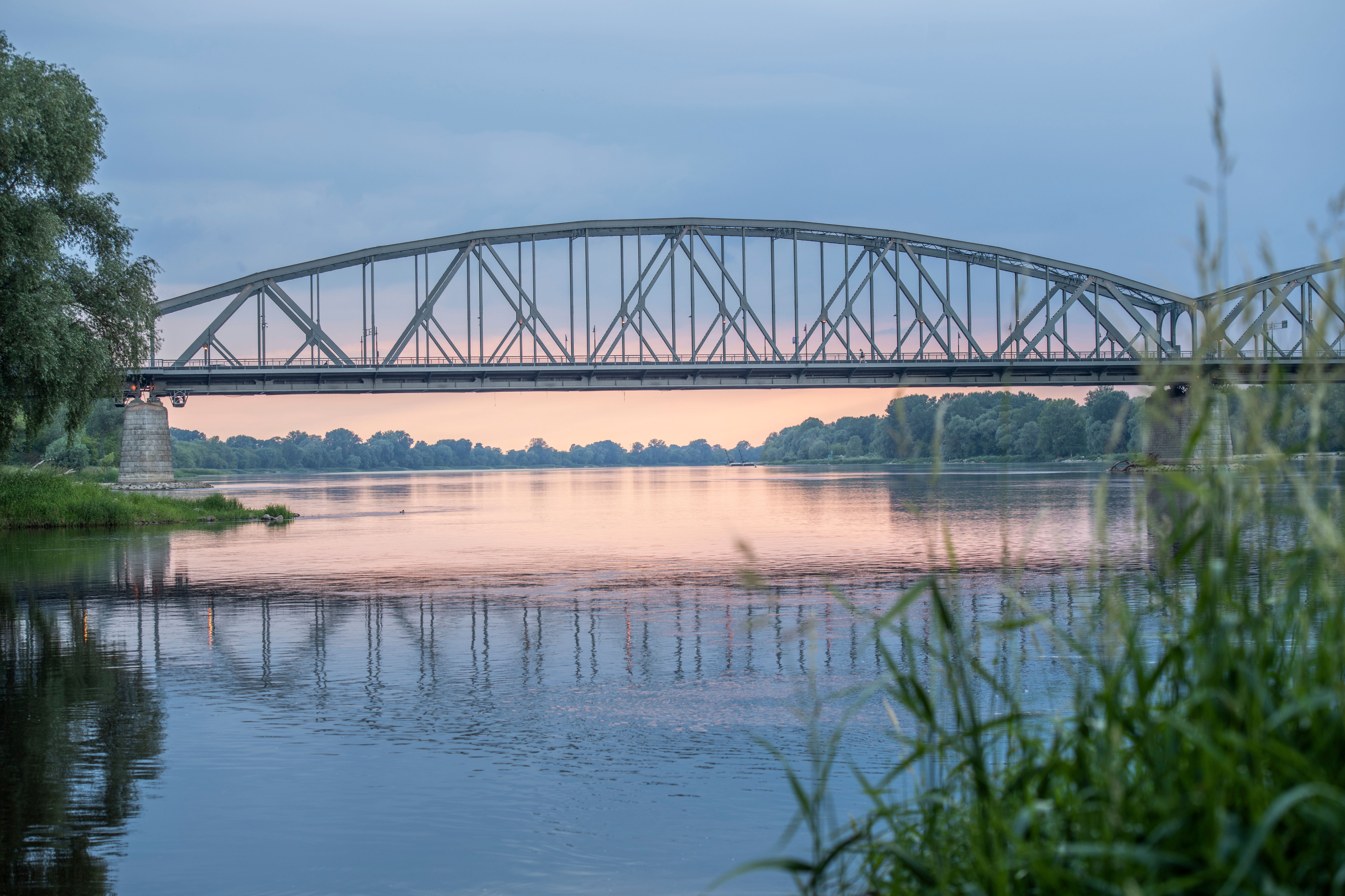 Peaceful view of a railroad bridge stretching across a calm river with a beautiful sunset backdrop.