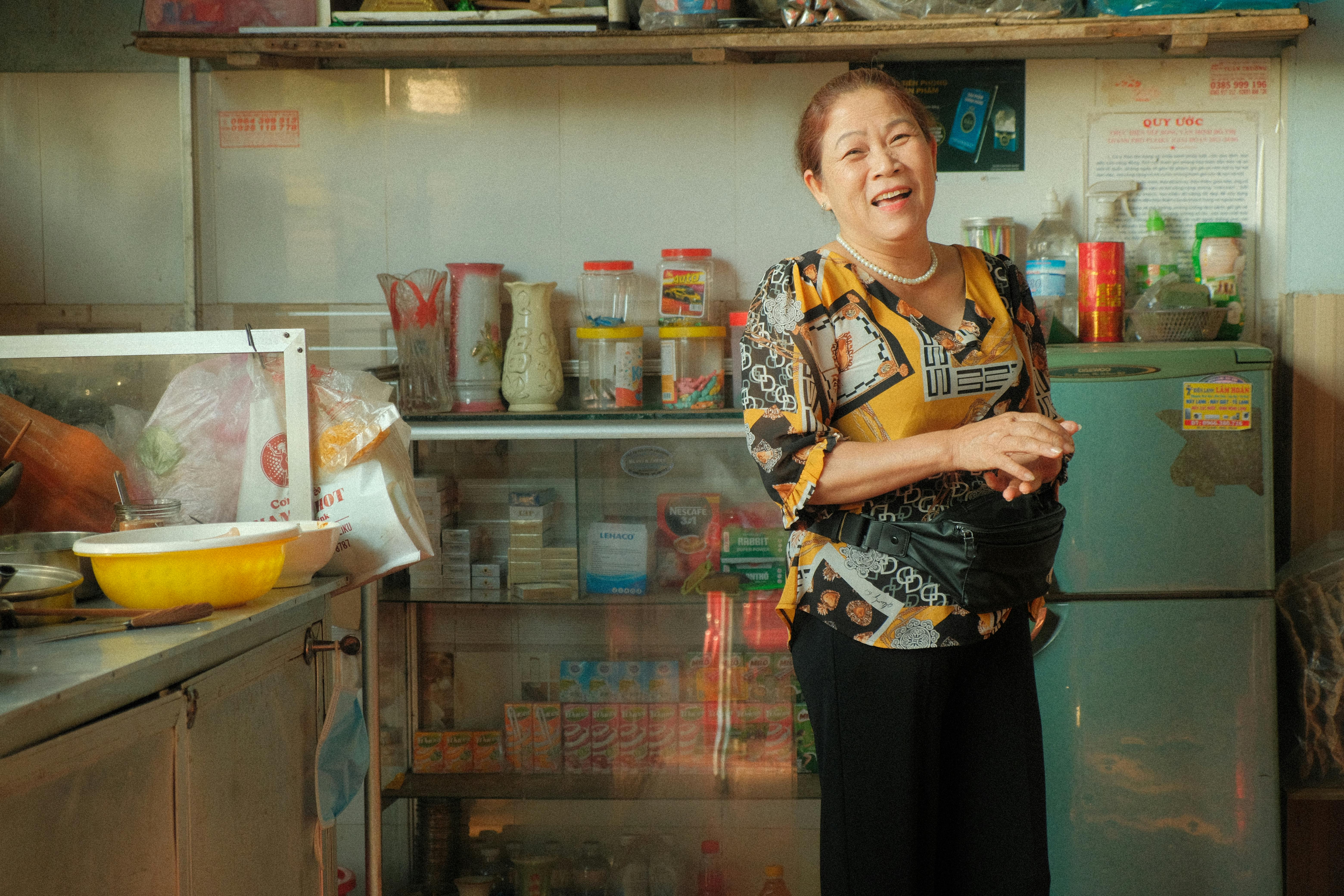 Joyful woman standing in a kitchen filled with colorful jars and bags, exuding warmth.