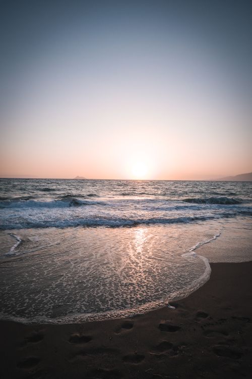 Free Capture of a serene sunset over a calm beach with gentle waves and vast sky. Stock Photo