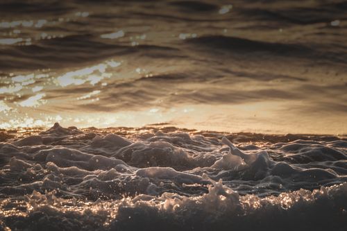 Free Foamy ocean waves reflecting the warm glow of a golden sunset, creating a serene seaside view. Stock Photo