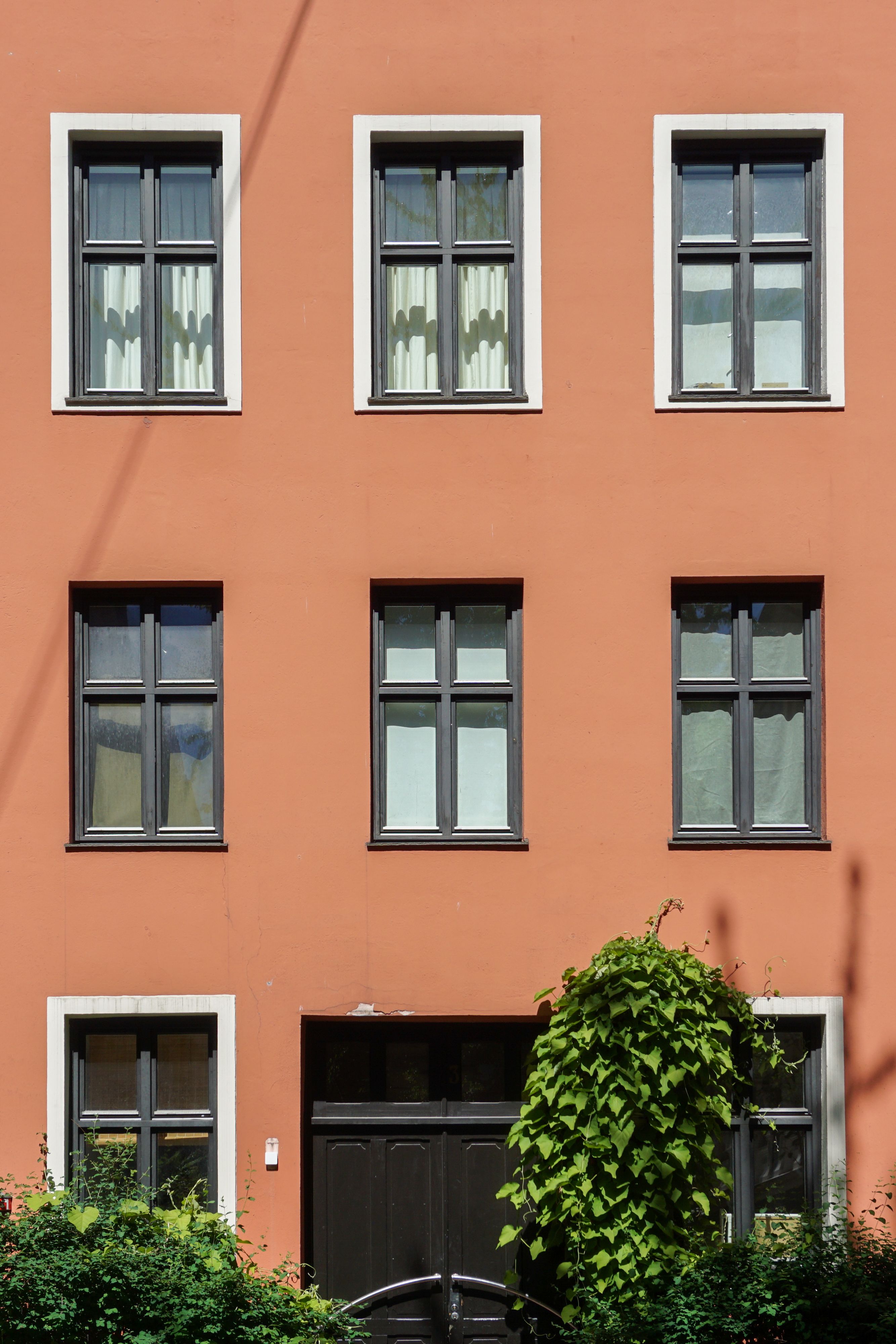 Free Vibrant orange townhouse facade in Oslo with symmetrical windows and lush greenery. Stock Photo