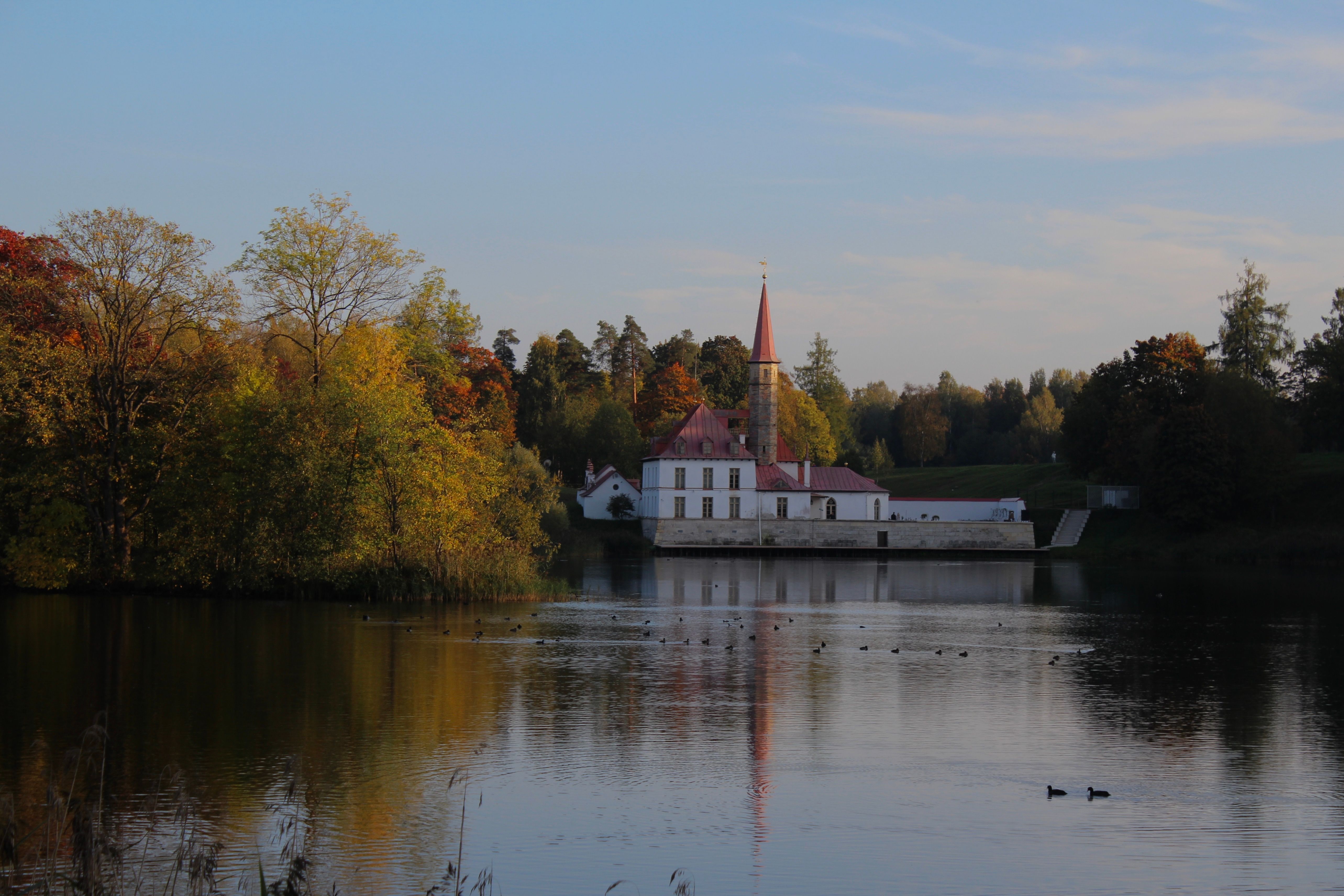 Reflective view of Priory Palace amidst autumn colors by the lake in Gatchina, Russia.