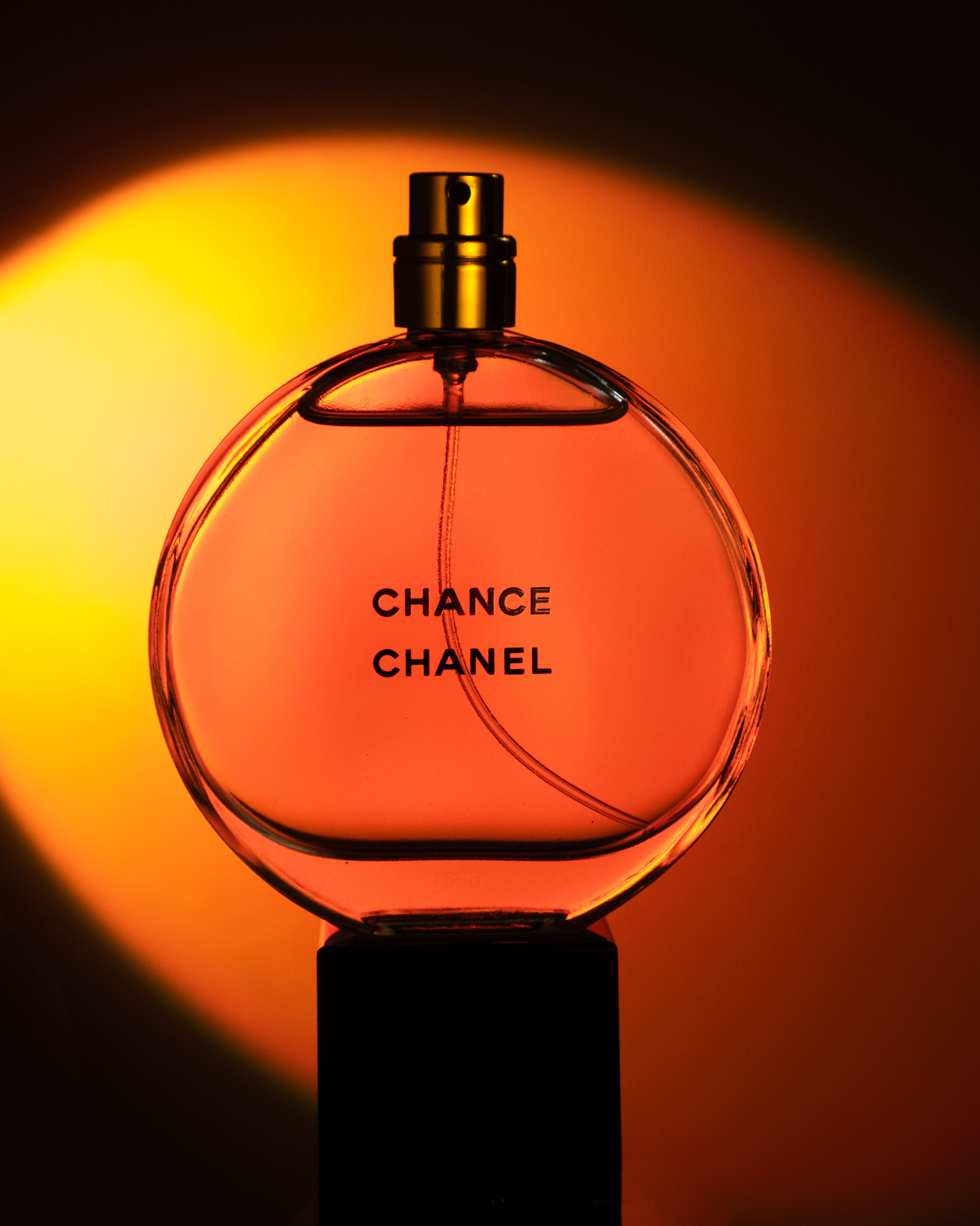 Elegant still life of Chanel Chance perfume bottle against vibrant orange background.