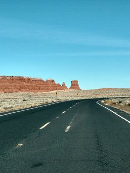 Empty highway cutting through Monument Valley's iconic desert landscape under a clear blue sky.