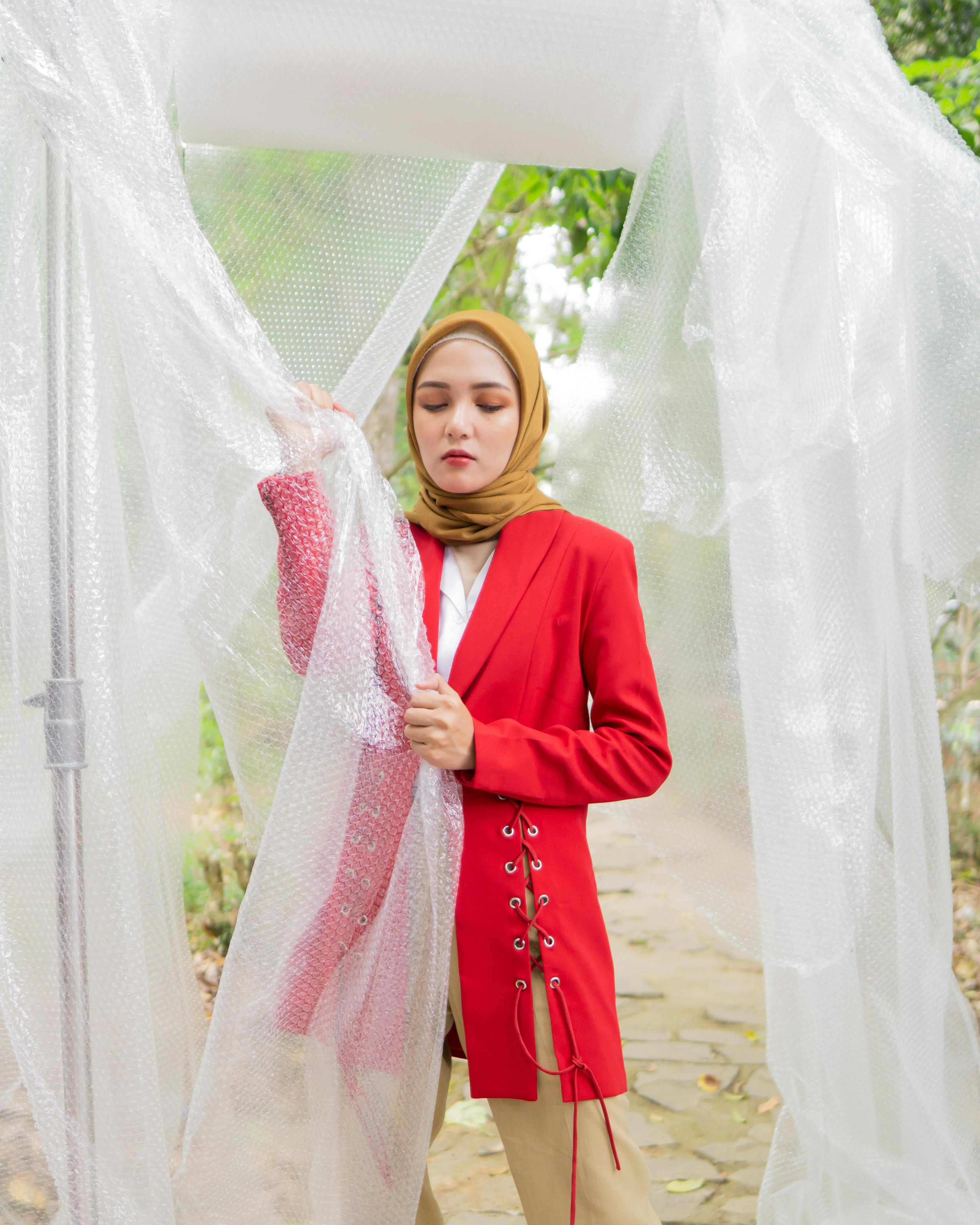 一位时尚女性身着红色西装外套，头戴头巾，站在创意户外布景中