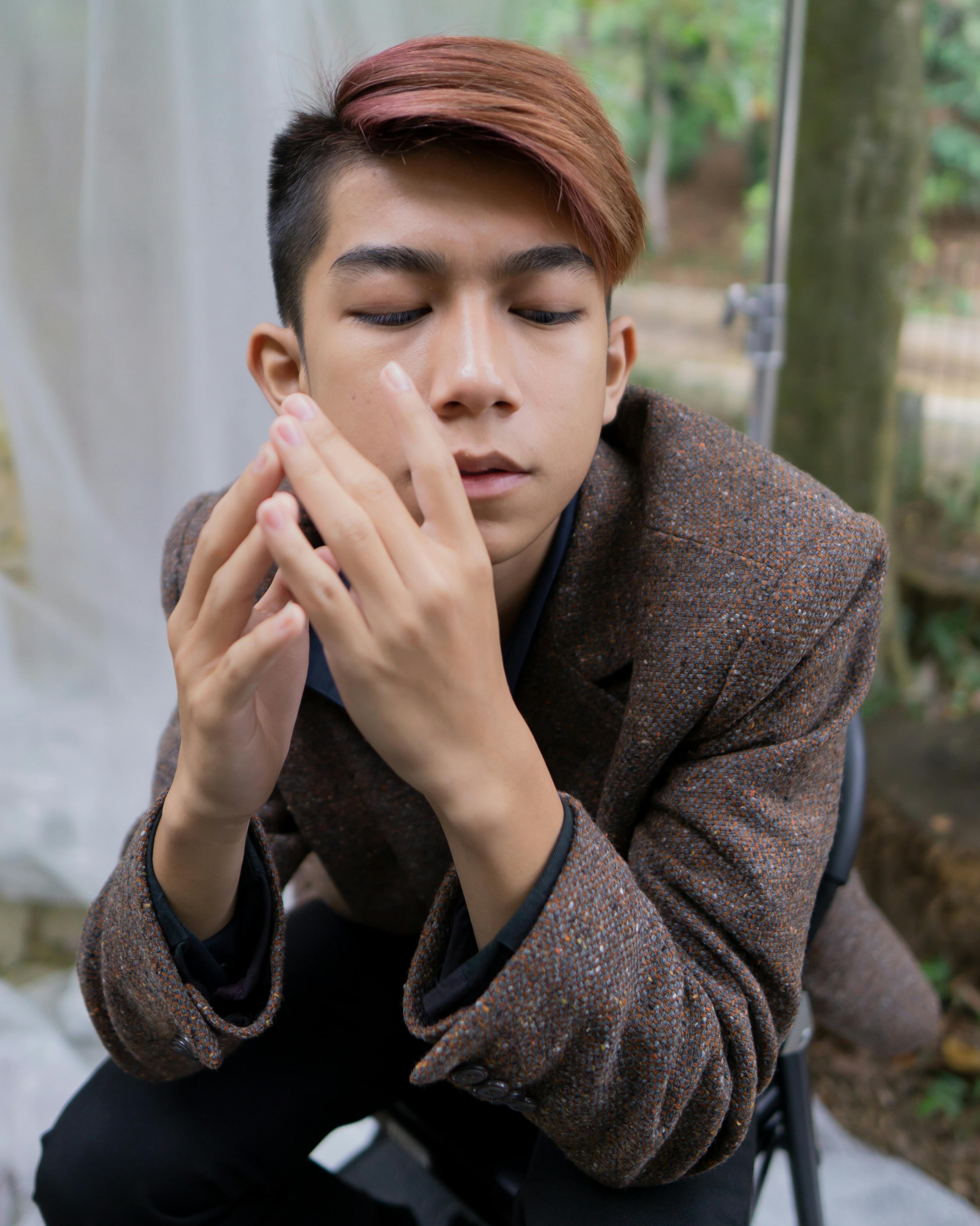 Stylish young man in a tweed coat posing outdoors with eyes closed.