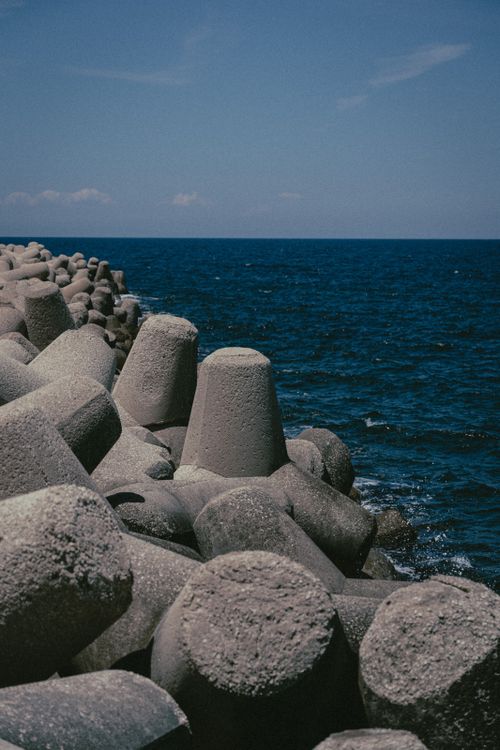 Free Concrete tetrapods on a breakwater edge the blue ocean under a clear sky in Italy. Stock Photo