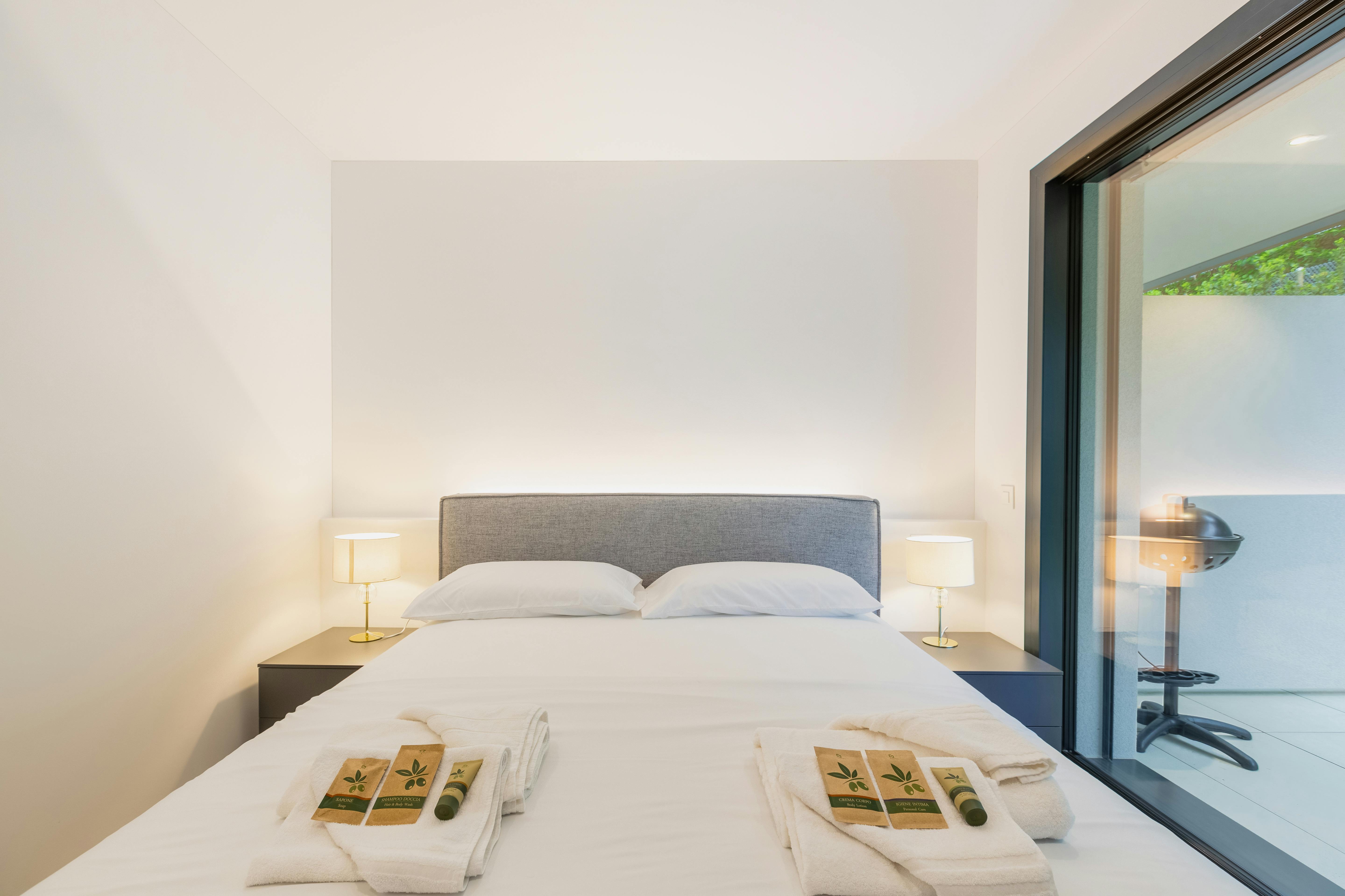 Modern minimalist bedroom with neutral tones, cozy bed, and balcony view; perfect for restful retreats.