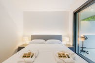 Modern minimalist bedroom with neutral tones, cozy bed, and balcony view; perfect for restful retreats.