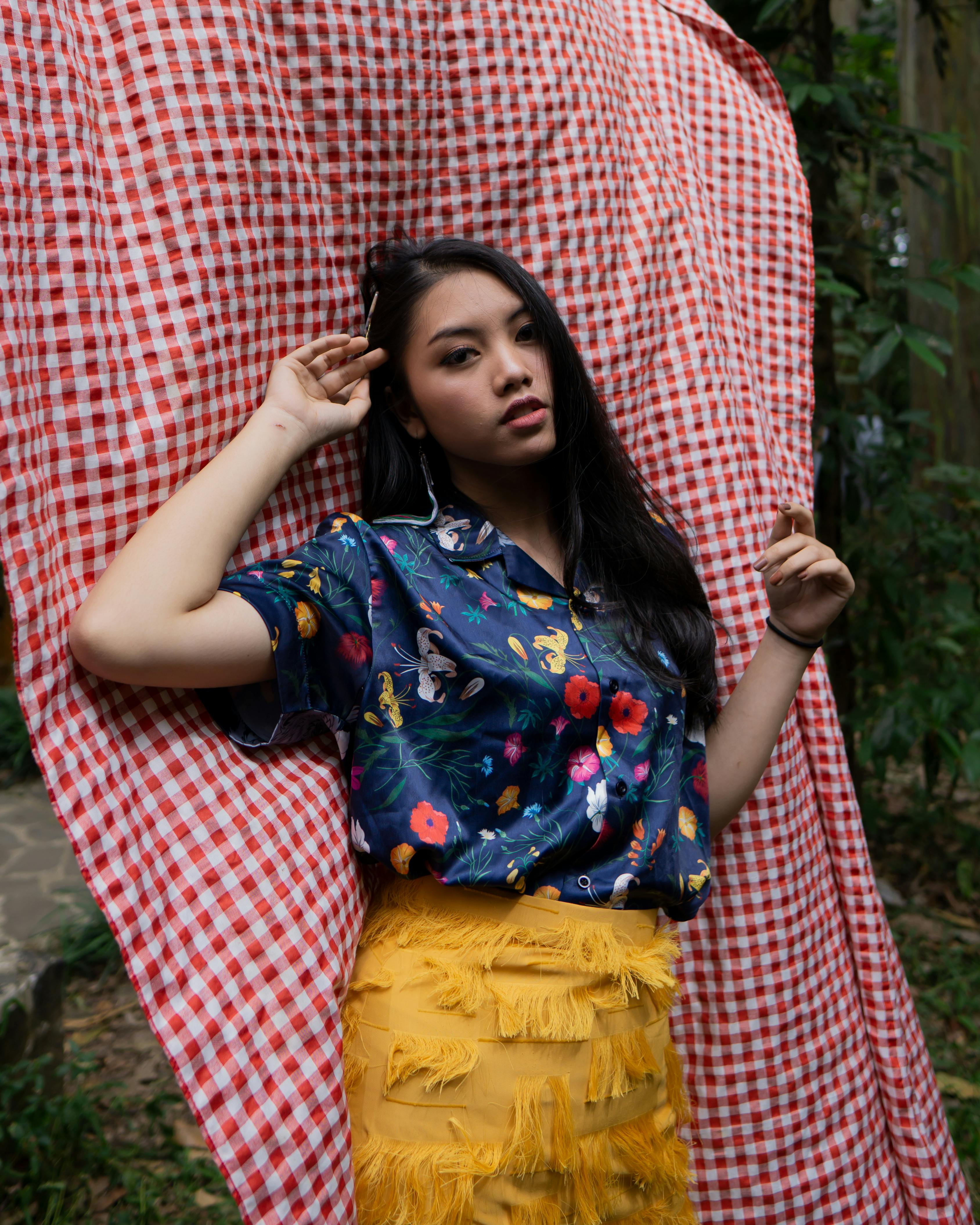 woman in blue and multicolored floral button up collared short sleeved shirt and yellow fringe skirt