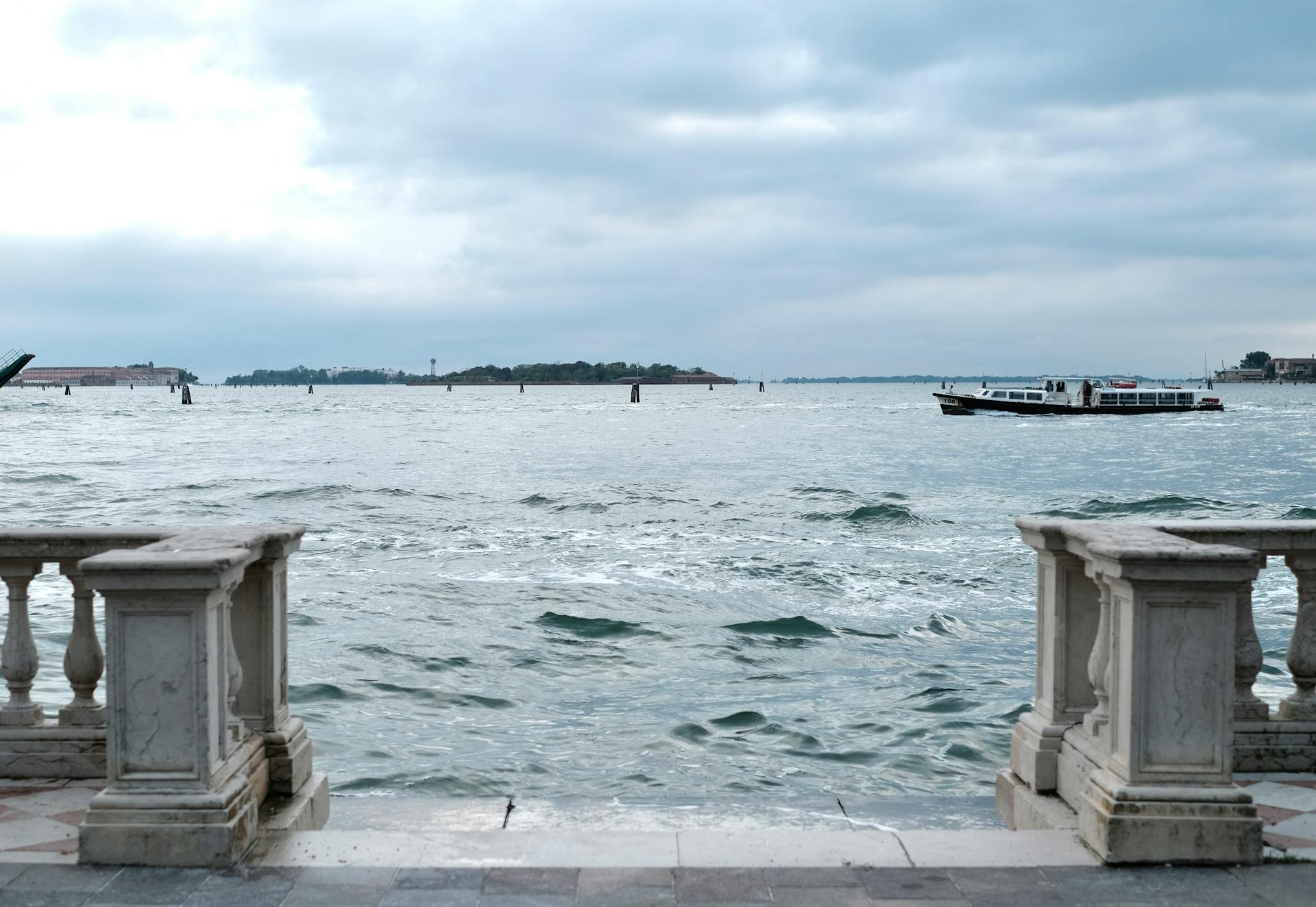 Tranquil seascape of a Venetian canal with a stone balustrade and overcast skies, showcasing typical Italian architecture.