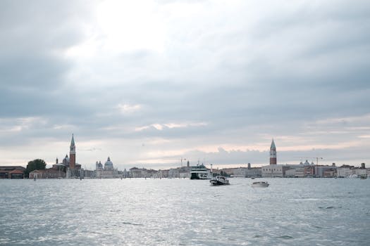 Serene waterfront view of Venice with iconic landmarks and motorboats under a cloudy sky.