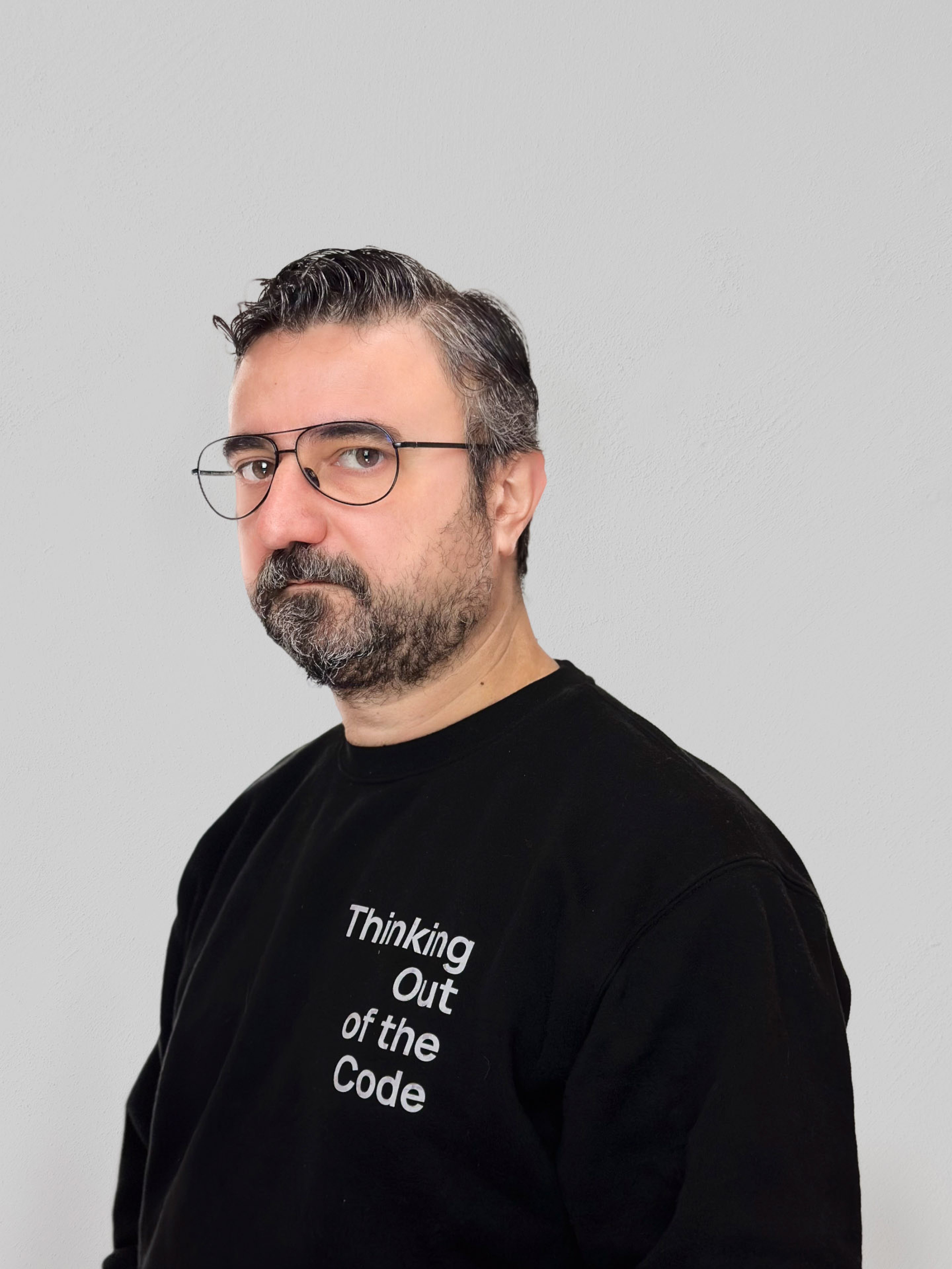 Bearded man wearing eyeglasses and a slogan sweater, looking thoughtful indoors.