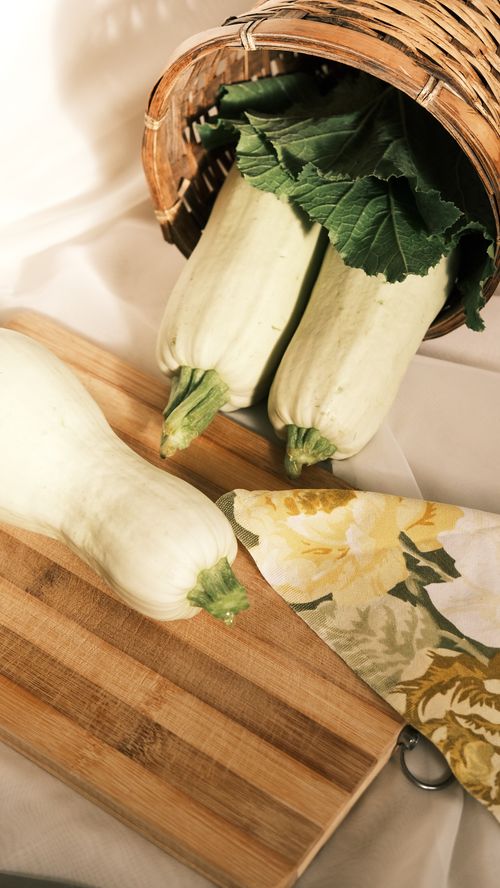 Free High angle view of fresh zucchinis on a wooden cutting board alongside a basket and cloth. Stock Photo
