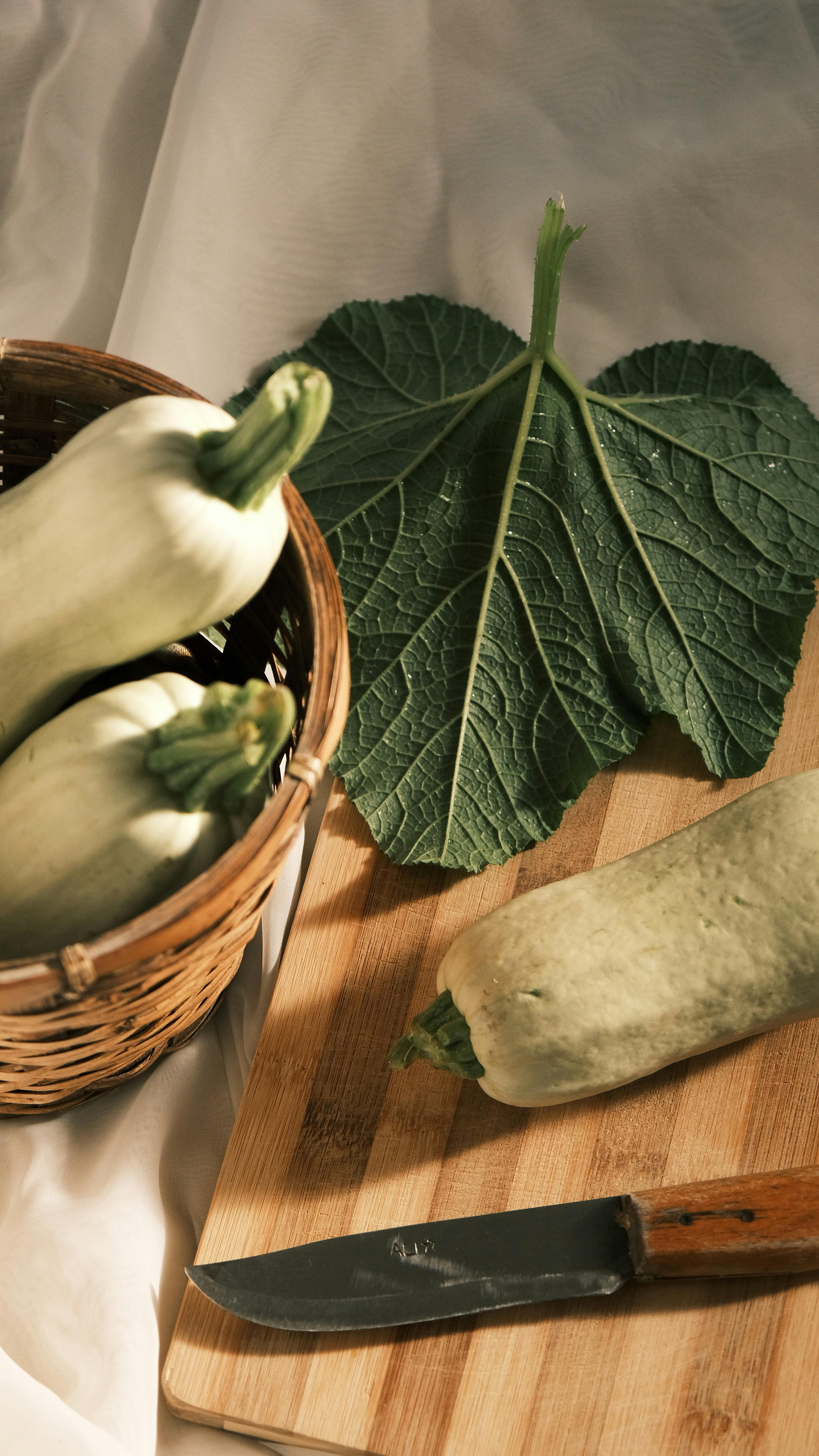 a basket with zucchini and a knife on a cutting board