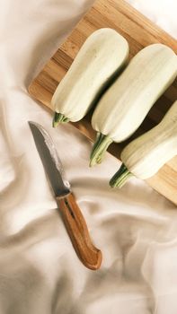 Three organic white zucchini arranged on a cutting board with kitchen knife, ready for preparation.
