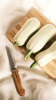 High-angle view of fresh white zucchinis on a cutting board with a kitchen knife.