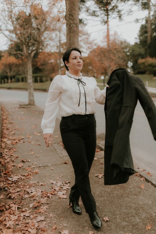 Free Elegant woman walking on an autumn street holding a coat, showcasing a stylish white blouse and heels. Stock Photo