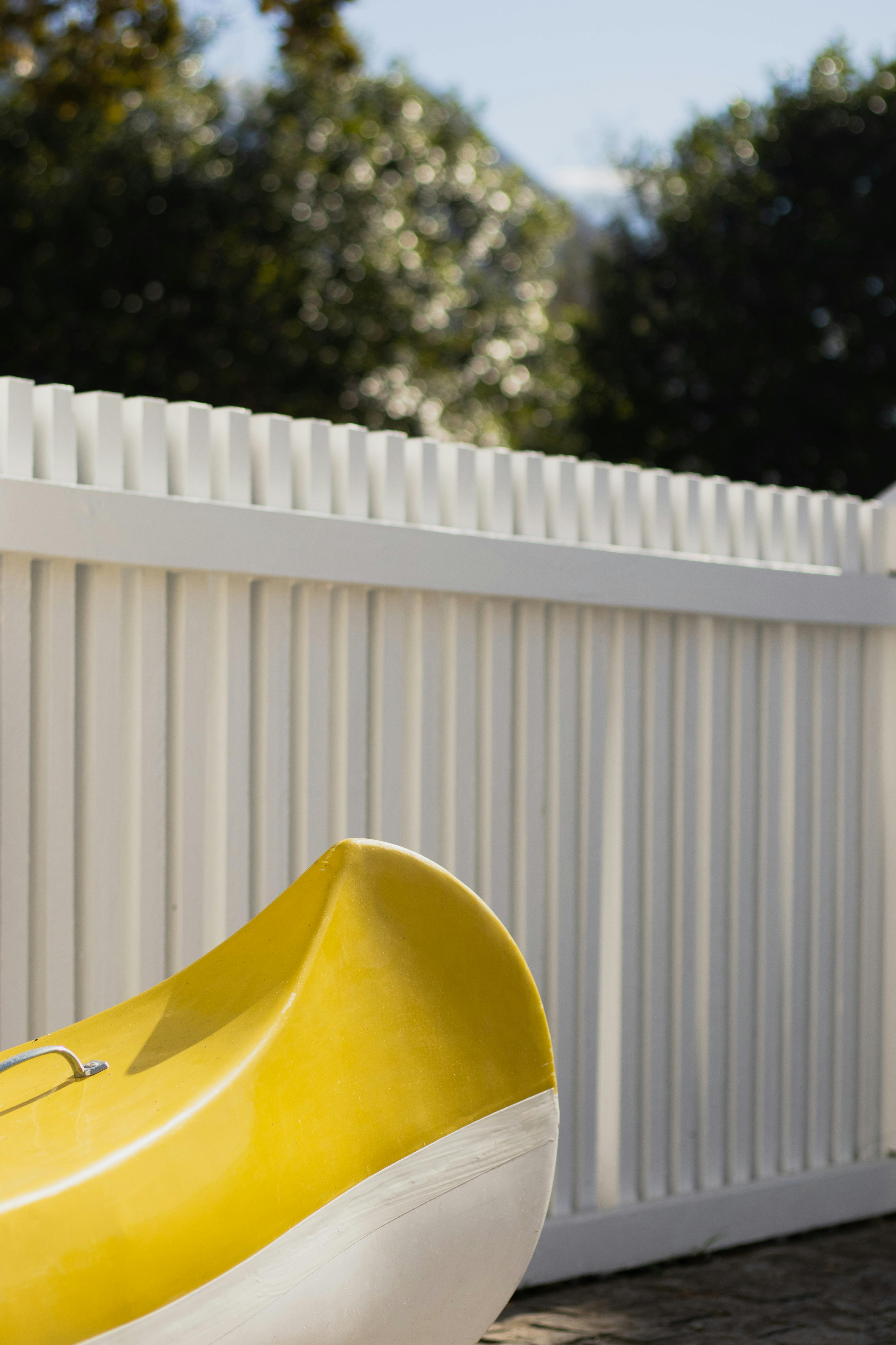 Bright yellow kayak against a white picket fence, evoking a summer day.