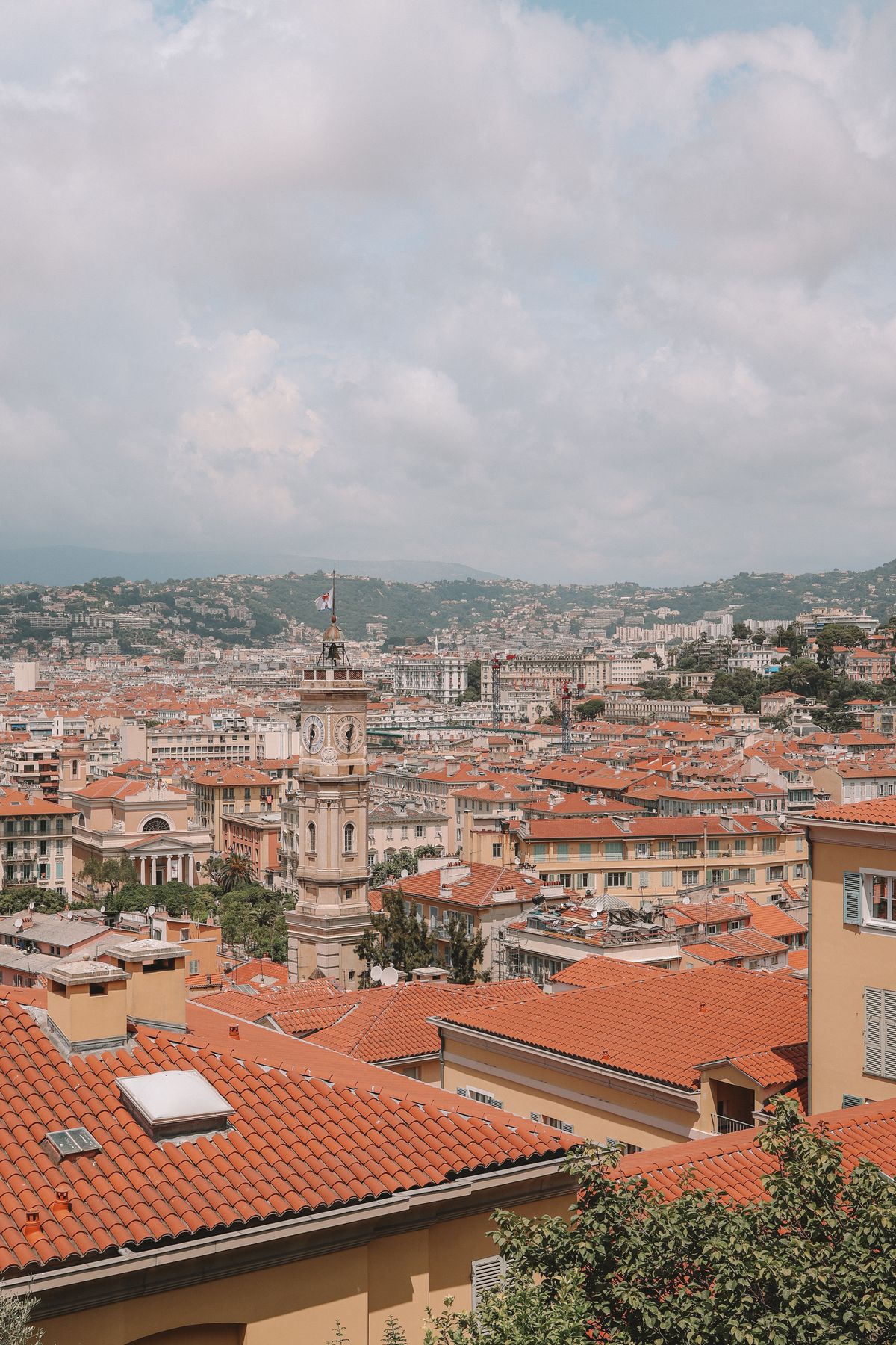 Os telhados vermelhos de Vieux Nice com a torre do relógio barroca e as colinas da Riviera ao fundo