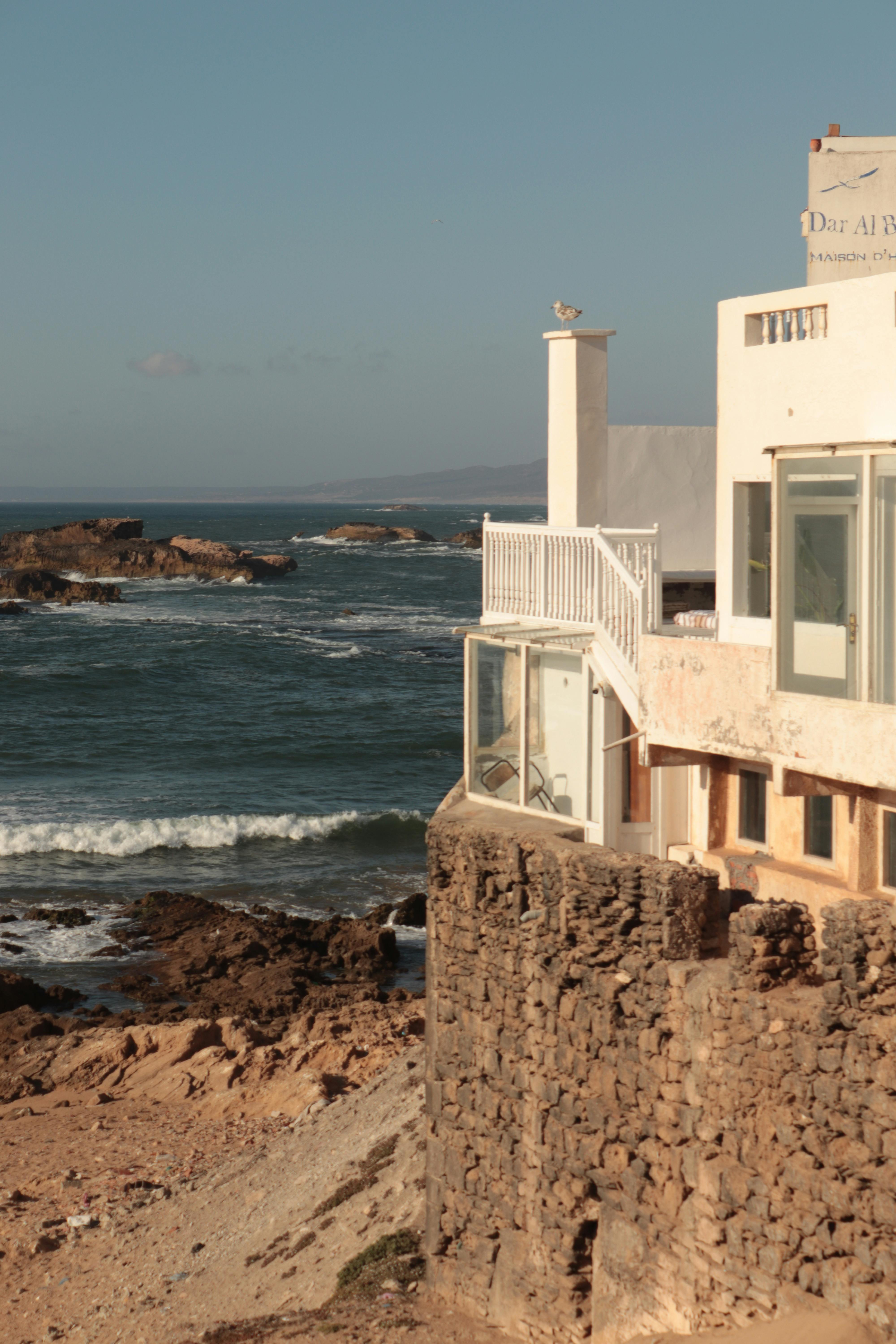 Charming oceanfront view of a house on the Moroccan coast with waves crashing below.
