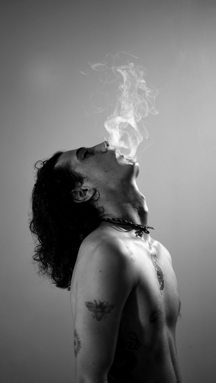 Black and white portrait of a man exhaling smoke in a studio setting, conveying a moody and dramatic atmosphere.