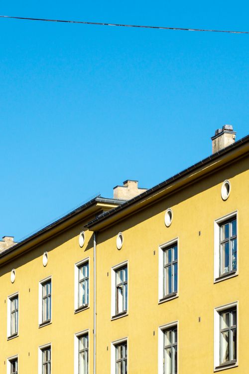 Free Bright yellow apartment facade in Oslo against a clear blue sky, showcasing Nordic architecture. Perfect for real estate. Stock Photo