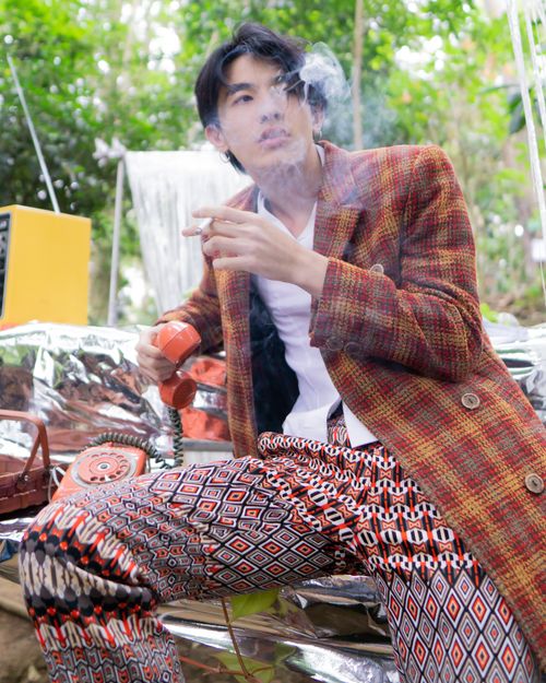Free Fashionable man in vibrant clothing smoking outdoors while holding an old telephone. Stock Photo