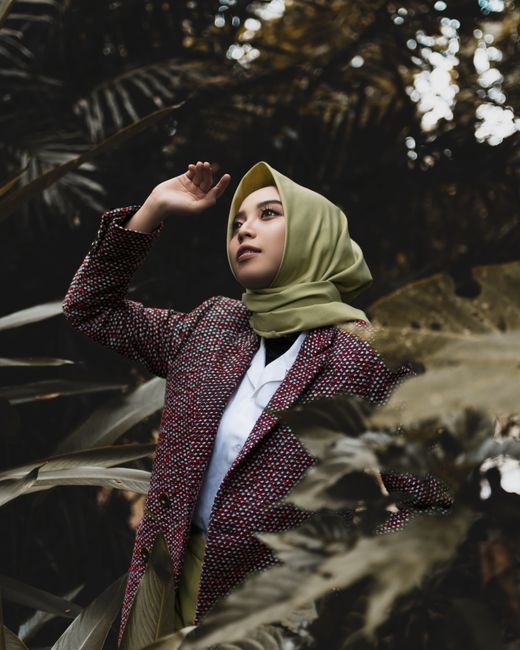 A fashionable woman posing outdoors in a hijab, surrounded by greenery in Jawa Barat, Indonesia.