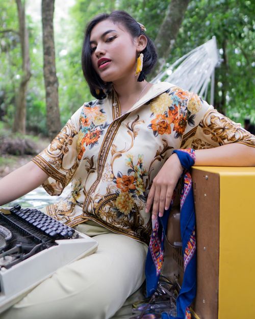 Free Fashionable woman in floral top posing outdoors with a typewriter in a lush green setting. Stock Photo
