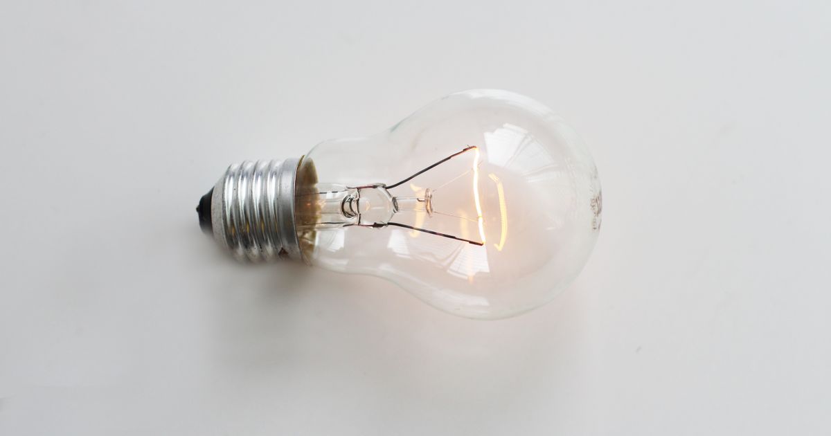 A close-up of an illuminated incandescent light bulb against a white background.