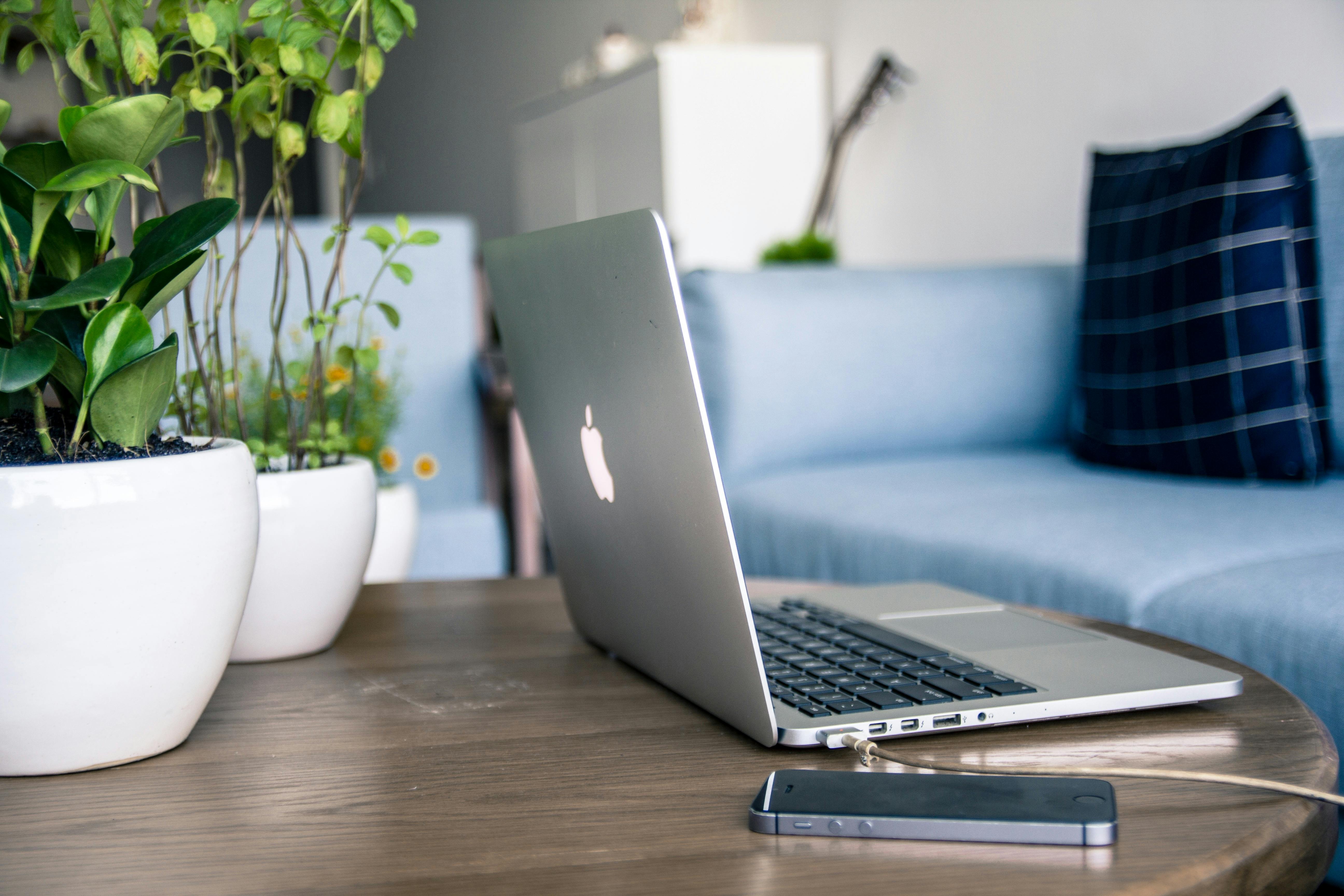 Open MacBook on a wooden coffee table with a smartphone and plants, symbolizing remote work opportunities and modern career life