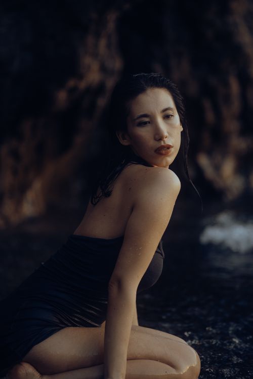 Free A serene portrait of a young woman kneeling by the sea, showcasing beauty and tranquility. Stock Photo