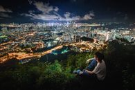 男人从山顶的栖息处，俯瞰着下方灯火通明的城市天际线，享受着令人叹为观止的夜间城市景观