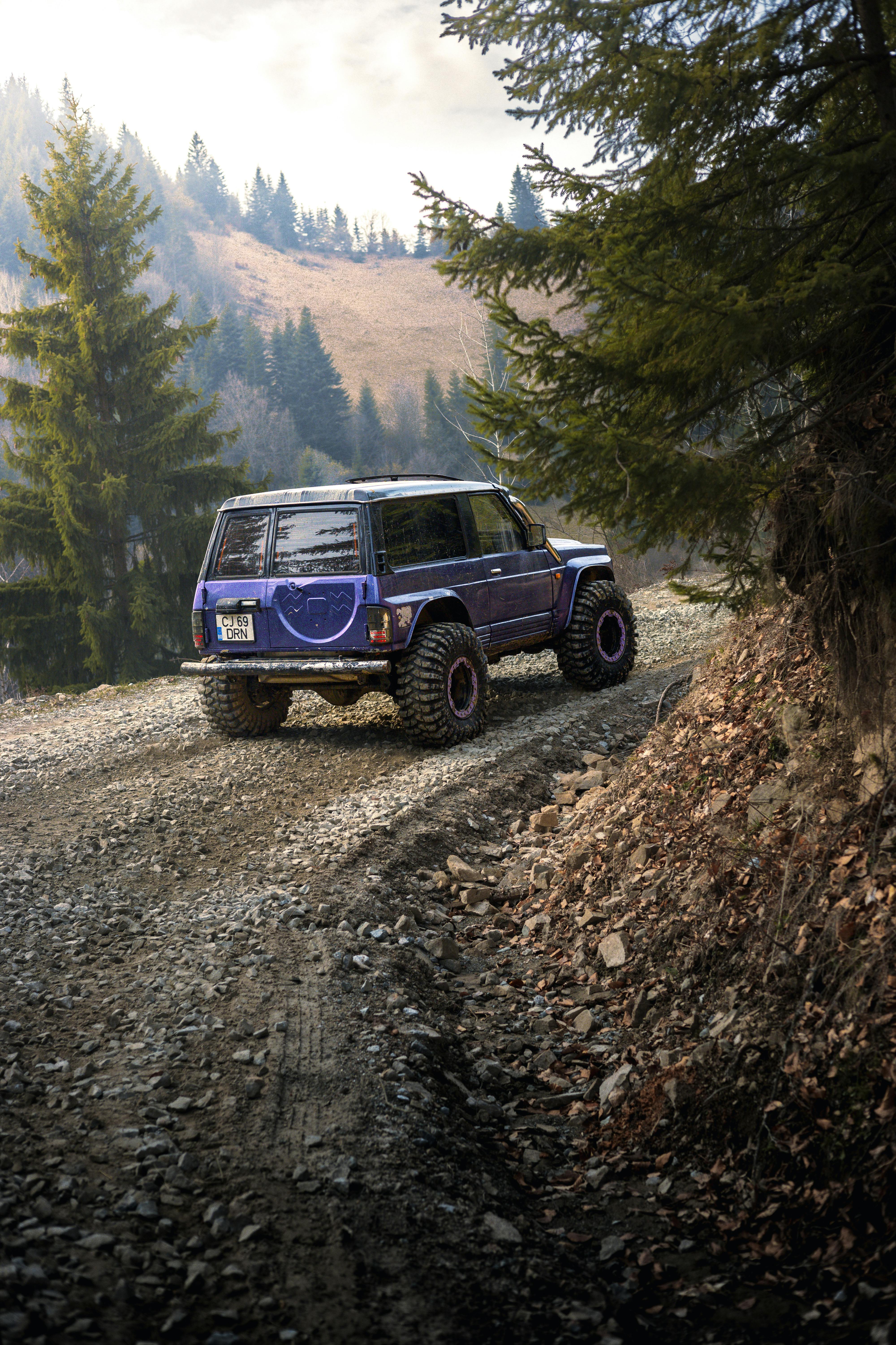 Blue SUV navigating a rugged mountain road in Romania, surrounded by coniferous forest.